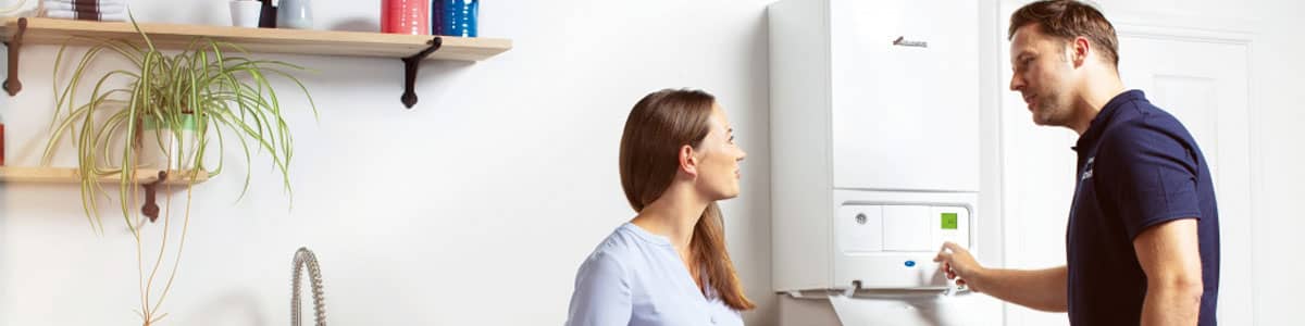 Woman having new boiler installed in kitchen by plumber